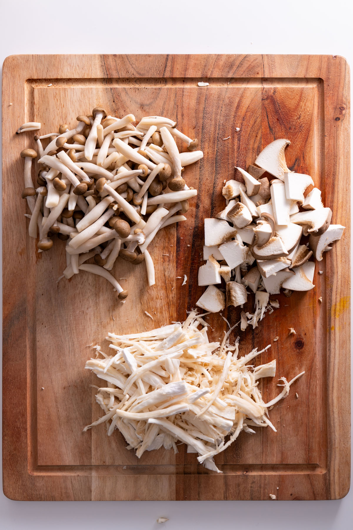 Chopped king oyster and shimeji mushrooms on a wooden cutting board.