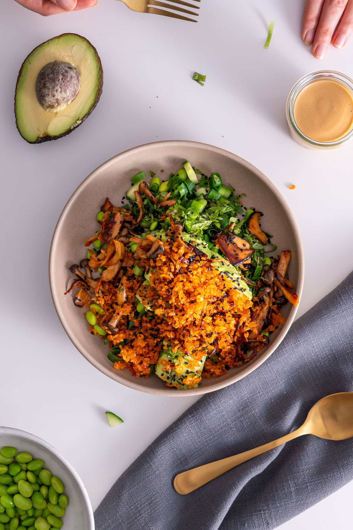 Top view of crispy rice salad with avocado, gochujang mushrooms, and edamame, next to avocado and peanut sauce.