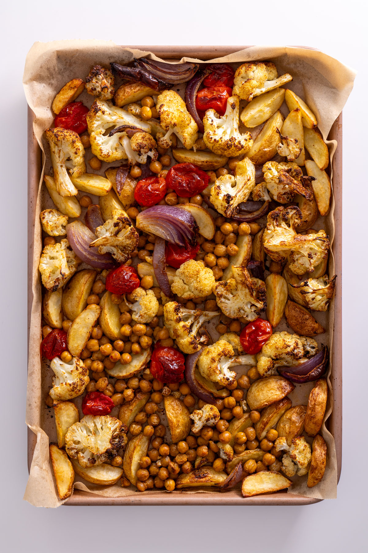 Roasted cauliflower, potatoes, chickpeas, and red onion on a baking tray fresh from the oven.