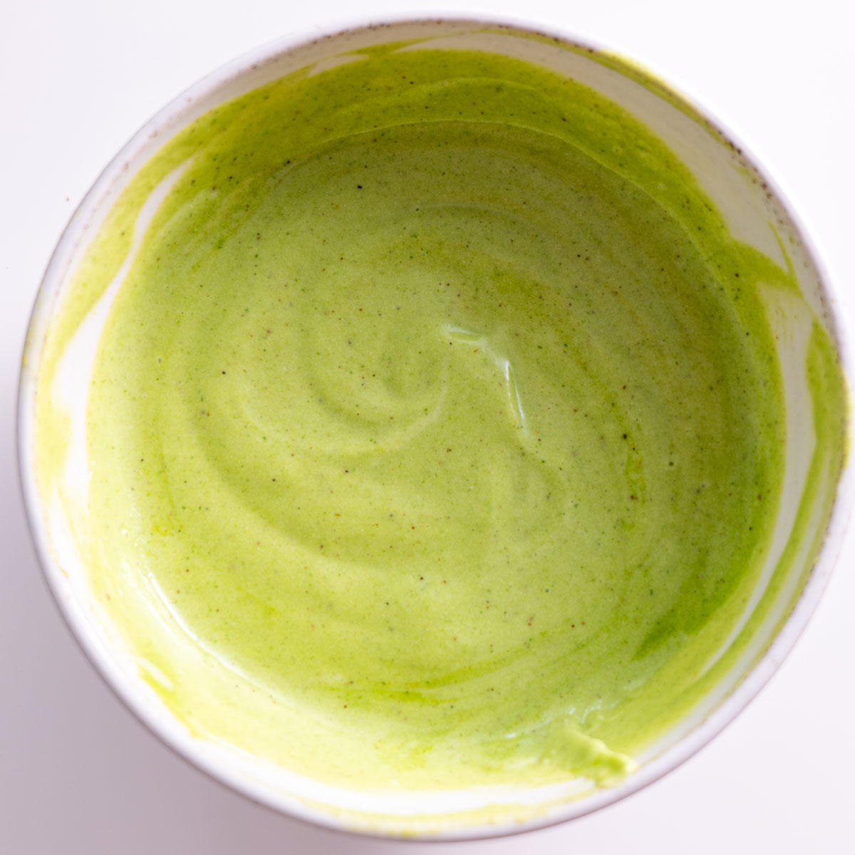 Raita sauce in a white bowl on a white surface, ready to serve with roasted vegetables.