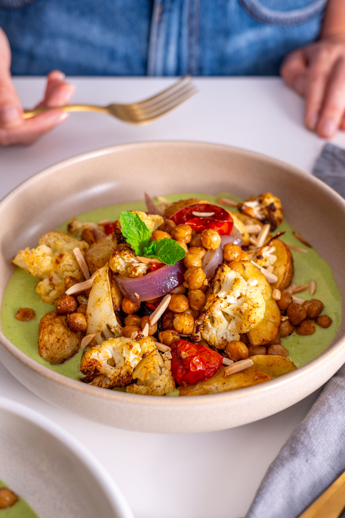 Sarah Cobacho holding a fork and about to enjoy a bowl of curry baked veggies with raita sauce.