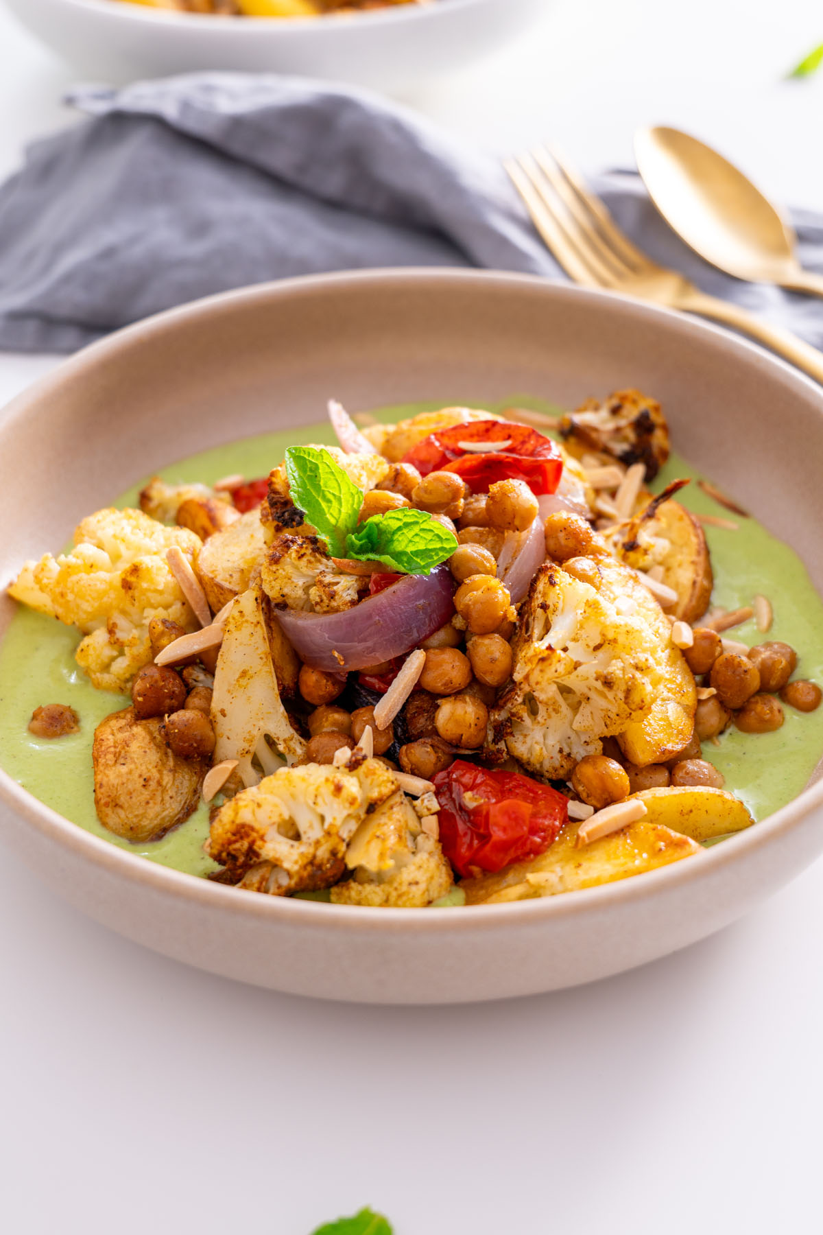 Close-up of roasted chickpeas, cauliflower, and red onion served with raita sauce.