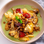 A serving of curry baked veggies with raita sauce, topped with mint and slivered almonds.