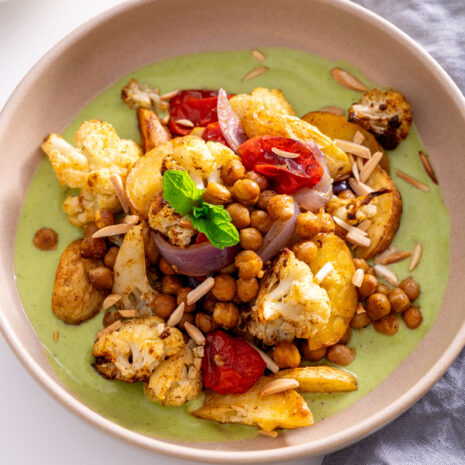 A serving of curry baked veggies with raita sauce, topped with mint and slivered almonds.