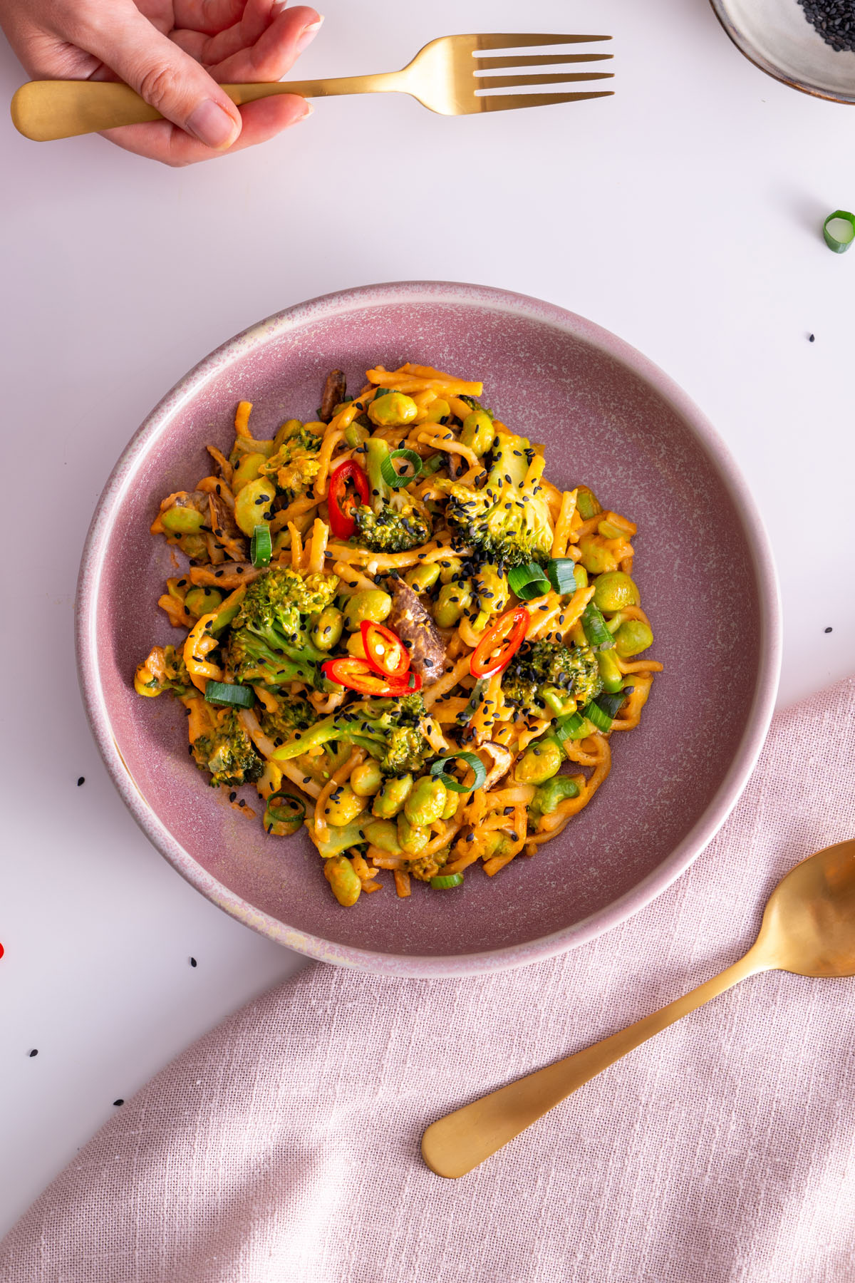 Overhead view of peanut gochujang noodles in a bowl with a golden fork.