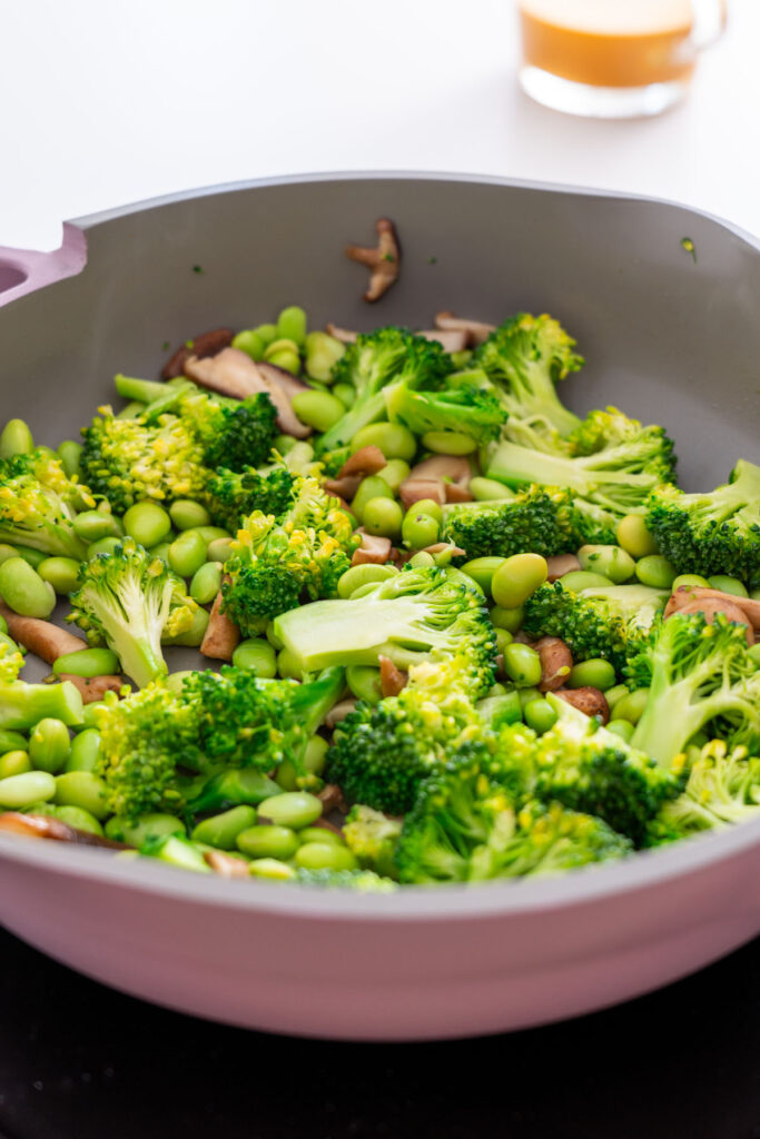 Stir-fried broccoli, edamame, and mushrooms in a pan for peanut gochujang noodles