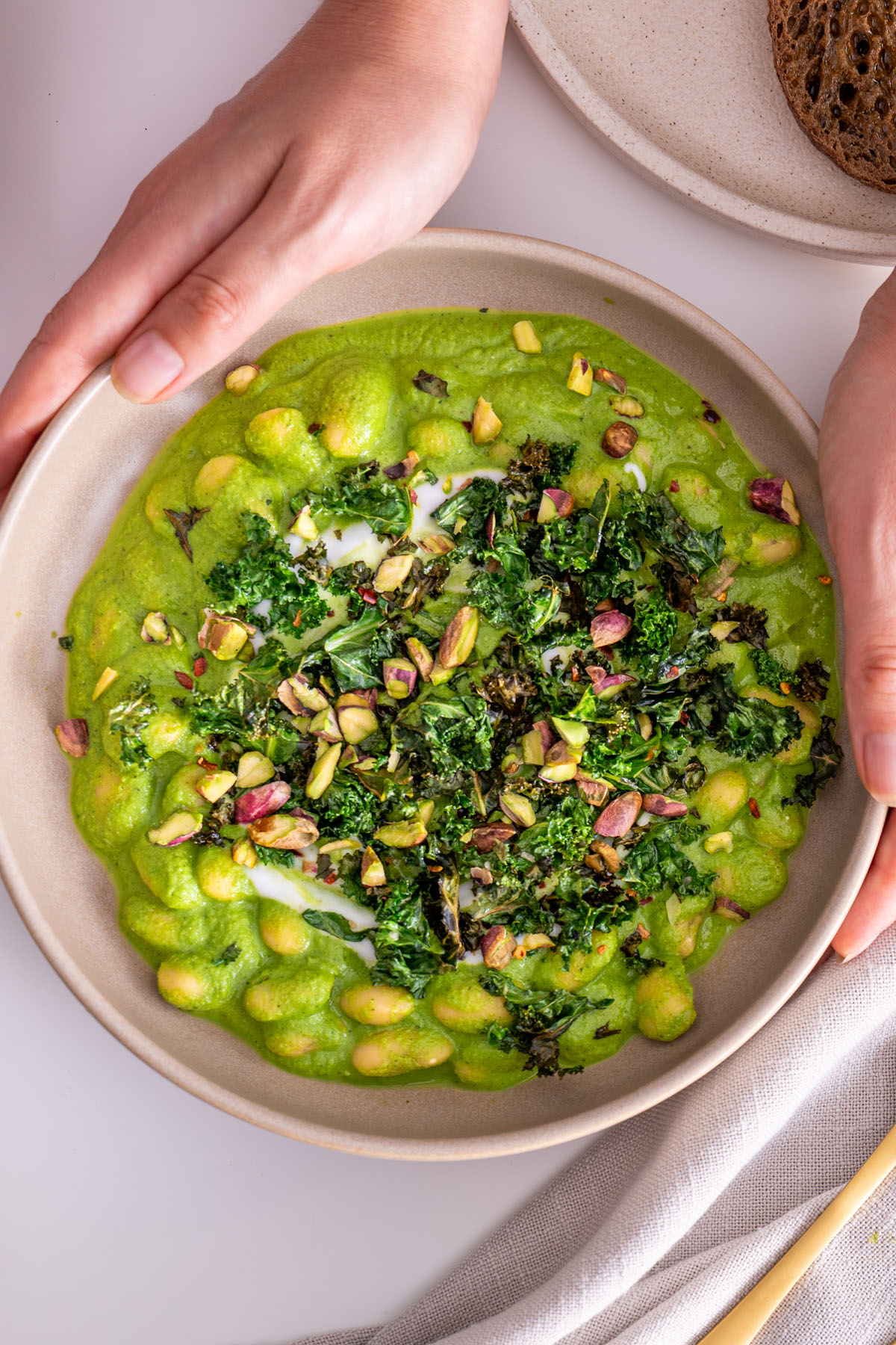 Super Green Butter Beans in a bowl, topped with crispy kale and pistachios, held by Sarah Cobacho