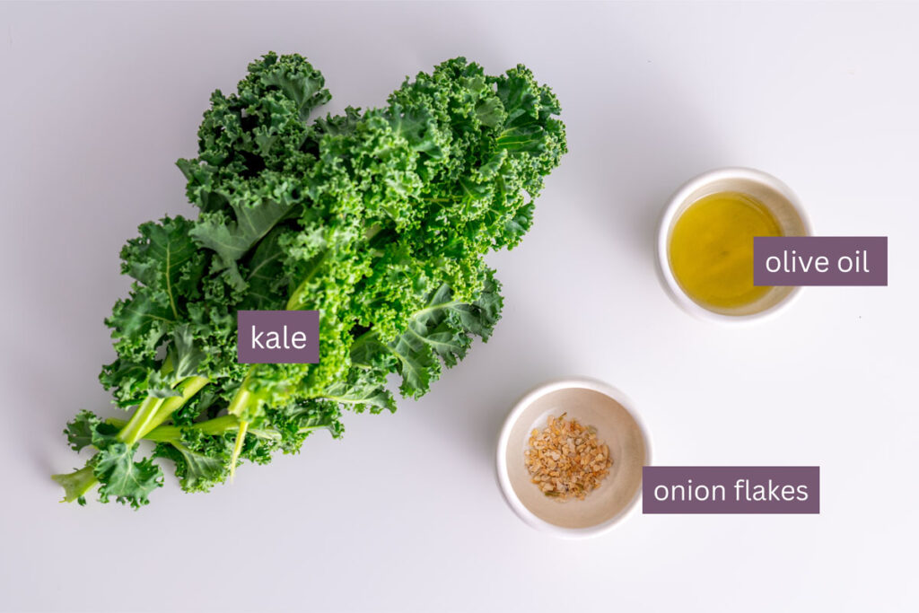 Fresh kale, olive oil, and onion flakes on a white surface for crispy kale topping