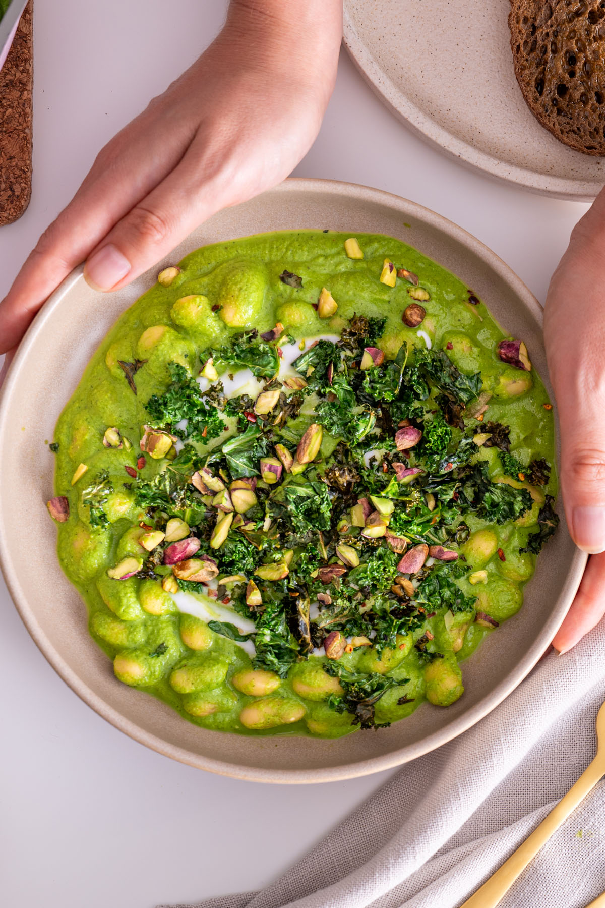 Super Green Butter Beans in a bowl, topped with crispy kale and pistachios, held by Sarah Cobacho