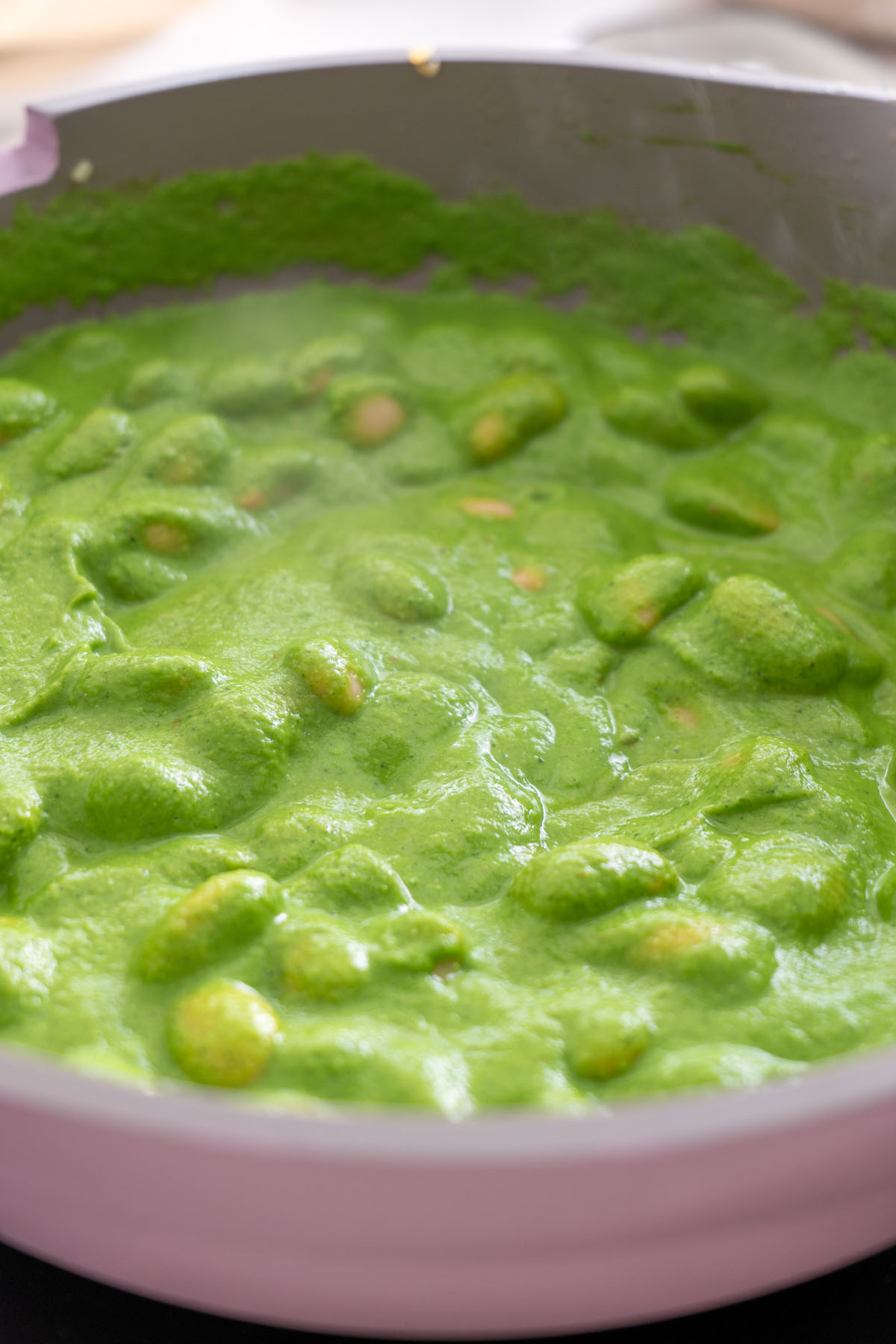 Close-up of Super Green Butter Beans simmering in a vibrant green sauce in a pan