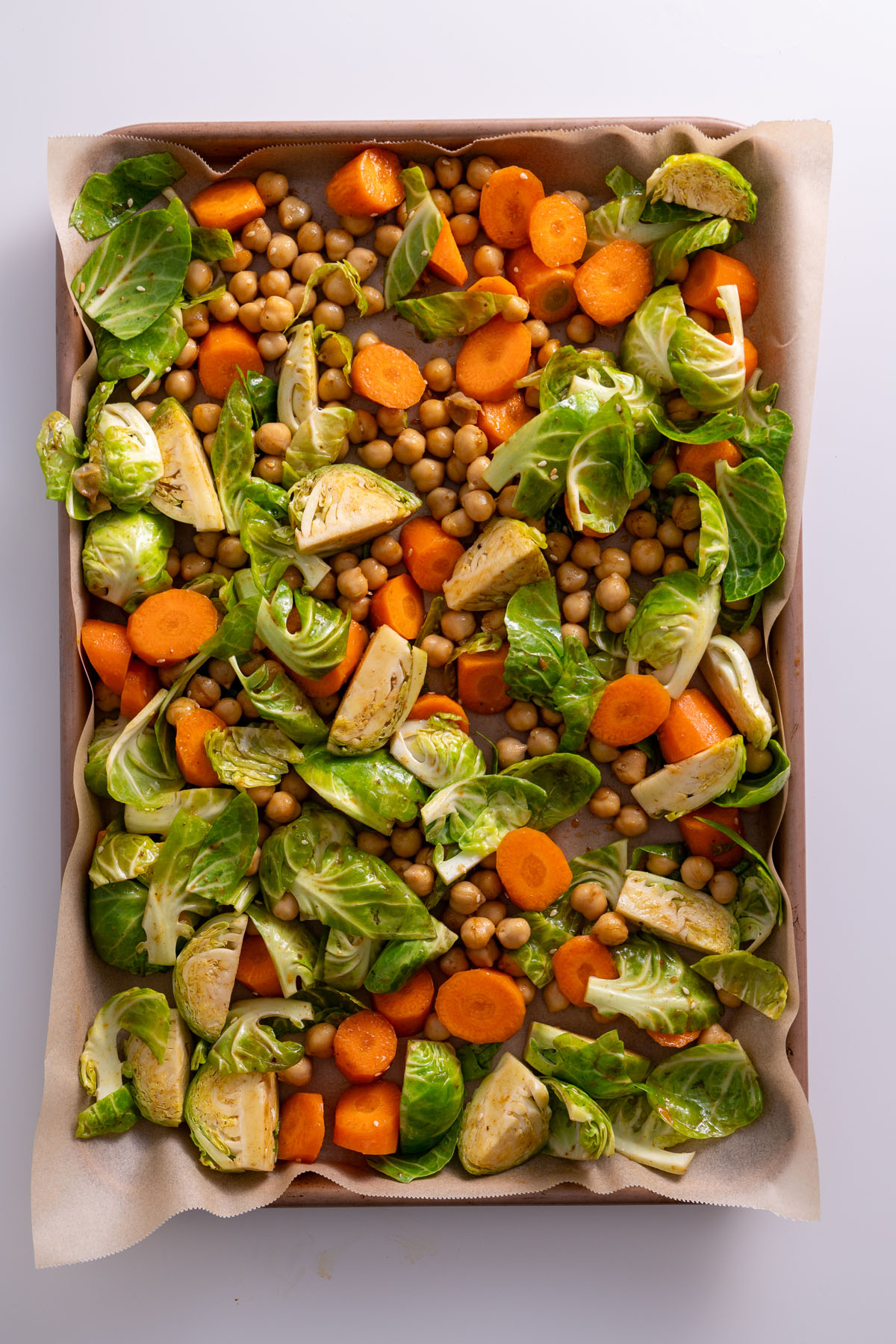 Chopped Brussels sprouts, carrots, and chickpeas on a baking tray ready for roasting.