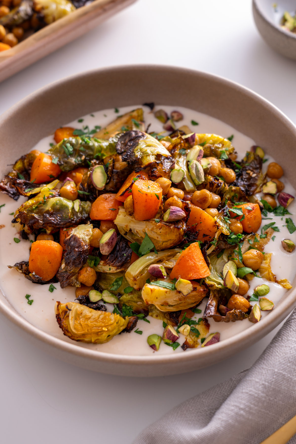 Roasted Brussels sprouts, chickpeas, and carrots on a plate with white bean spread, garnished with fresh coriander and pistachios.