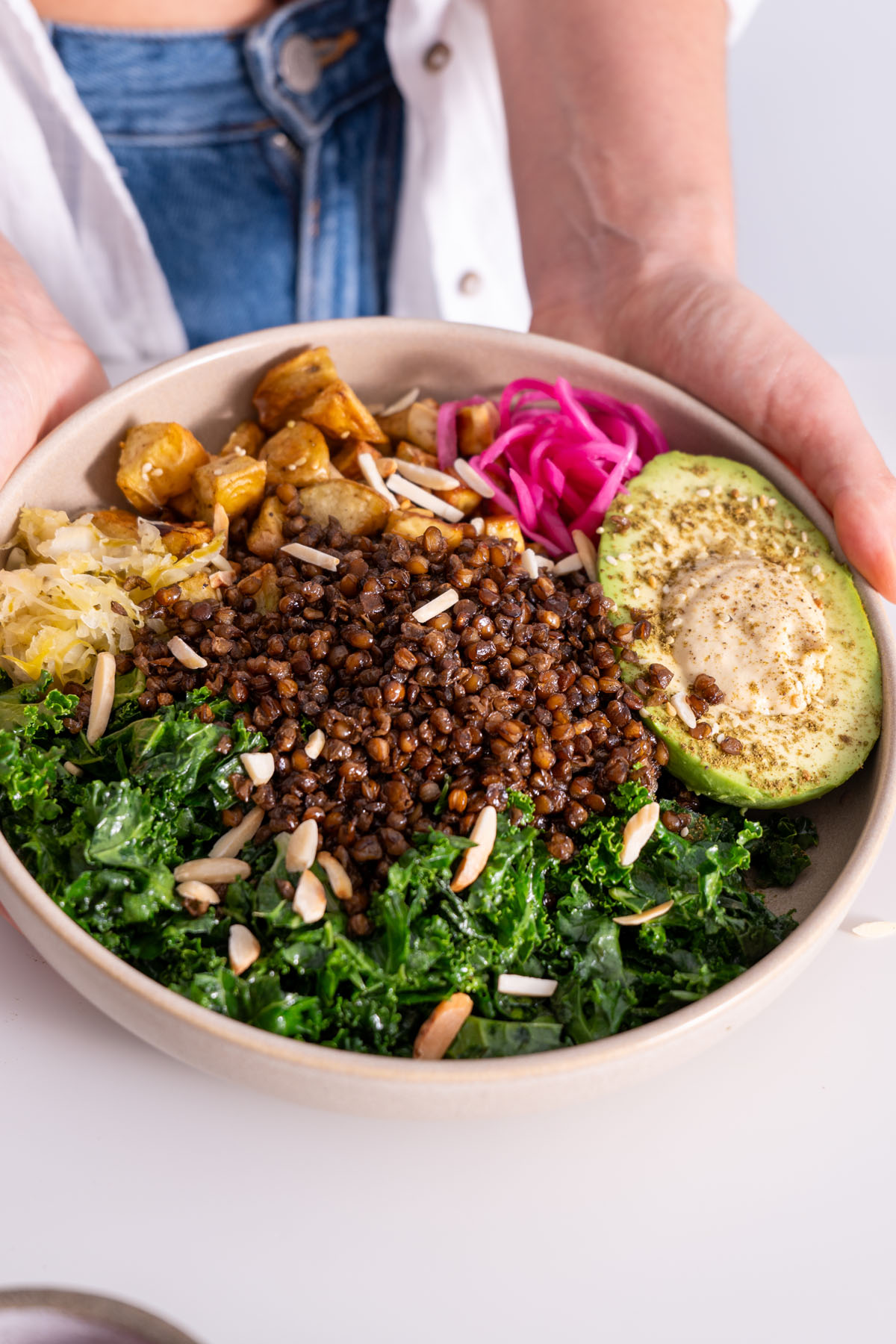 Close-up of Sarah Cobacho holding a vibrant bowl of crispy lentils, roasted potatoes, avocado, and kale.