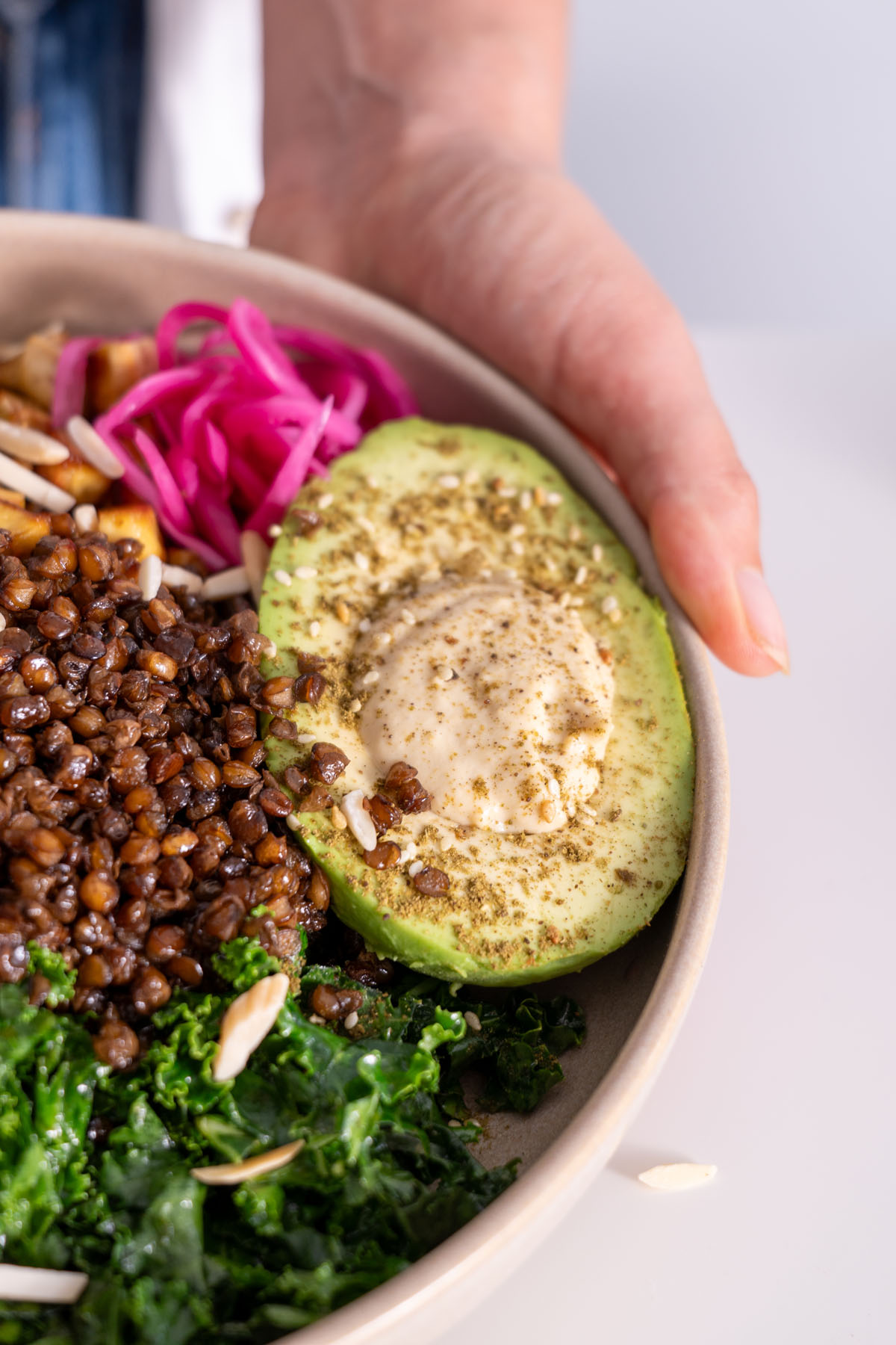 Close-up of an avocado half topped with hummus and seasonings, part of the crispy lentil and potato bowl.