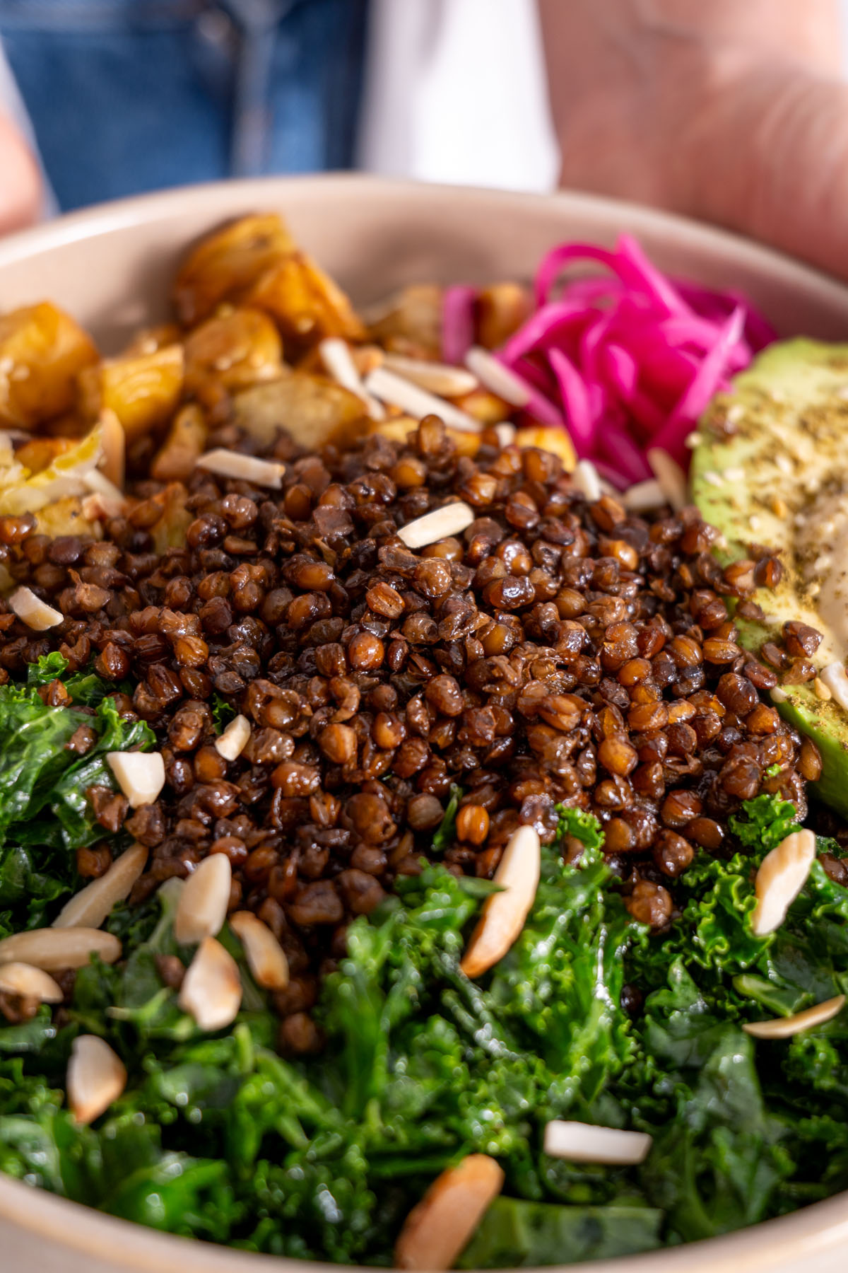 Close-up of crispy roasted lentils on top of a kale salad with avocado, pickled onions, and almonds.