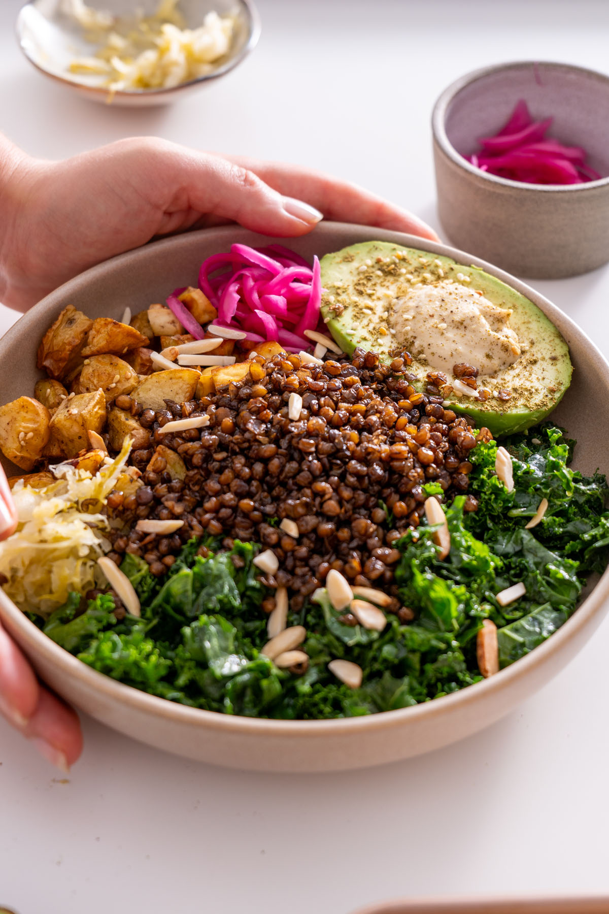 Sarah Cobacho adjusting a bowl filled with crispy lentils, roasted potatoes, avocado, and pickled onions.