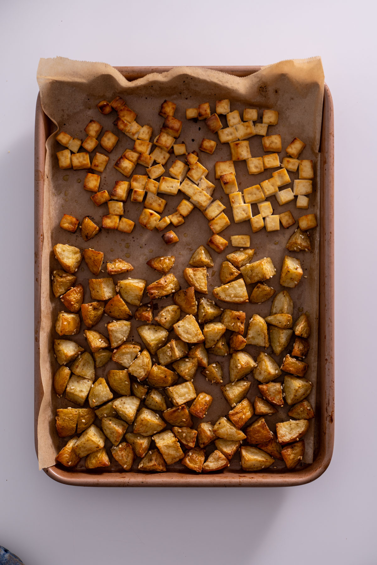 Tofu and potato cubes fully roasted on a baking sheet, golden brown and crispy.