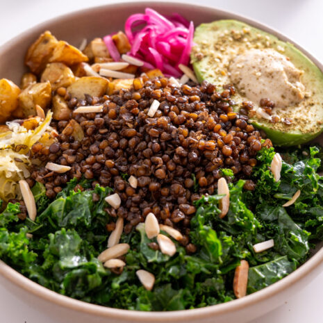 Crispy lentil and potato bowl assembled with kale, avocado, hummus, pickled onions, and almonds.