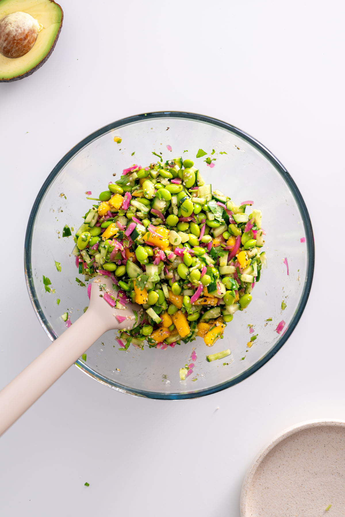 Close-up of the colorful topping mix with edamame, mango, cucumber, and pickled onions in a mixing bowl.