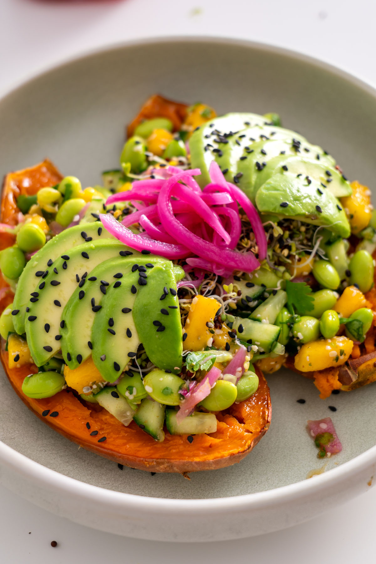Edamame Sweet Potato Bowl with vibrant toppings, including sliced avocado, black sesame seeds, and pickled onions, served on a light surface.