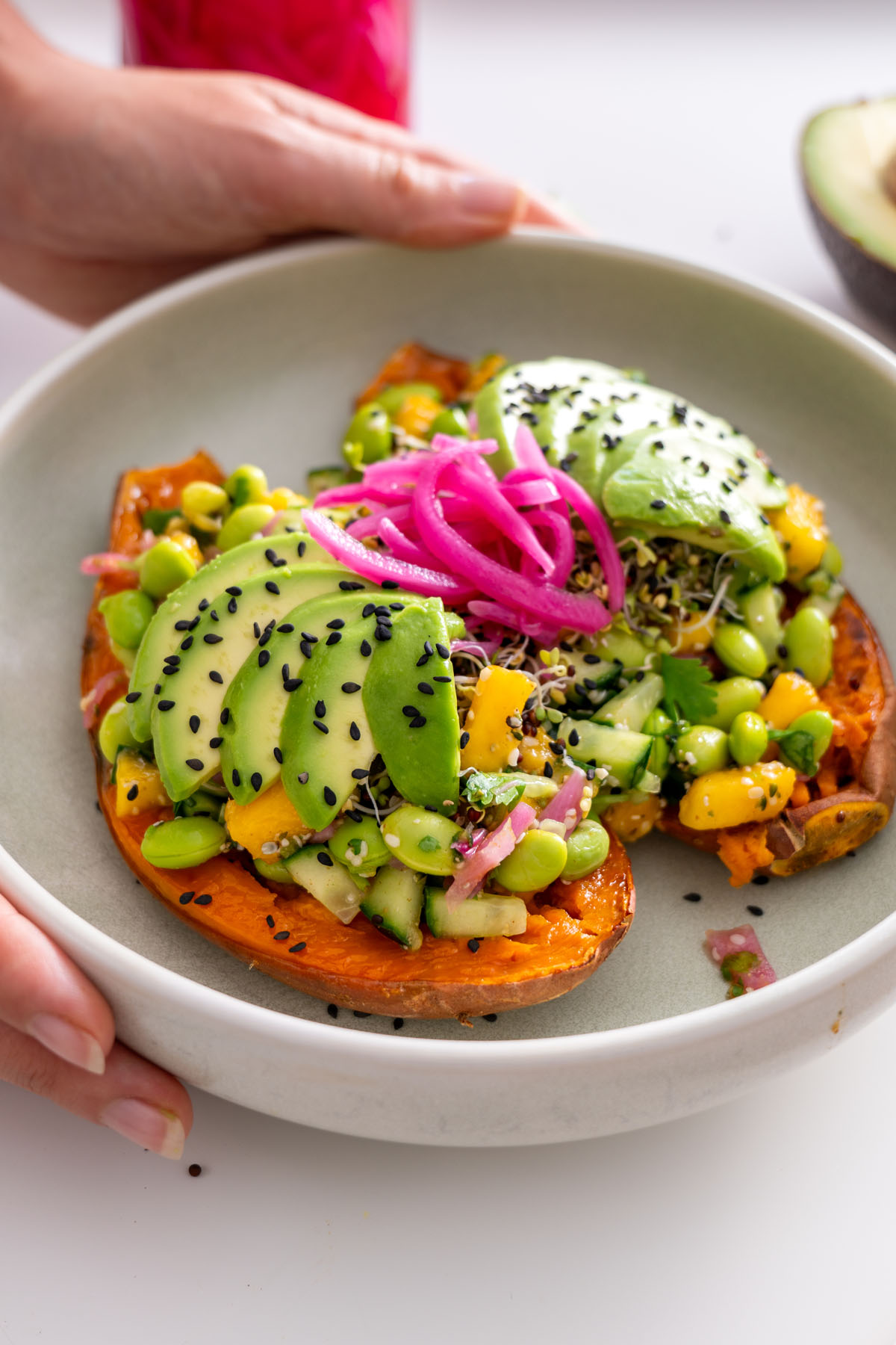 Close-up of roasted sweet potato with avocado, edamame, mango, and other fresh toppings in the Edamame Sweet Potato Bowl.
