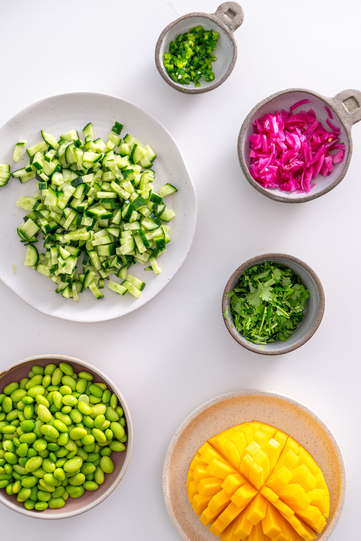 Edamame Sweet Potato Bowl ingredients prepped and displayed in individual bowls, showing edamame, cucumber, cilantro, mango, and more.