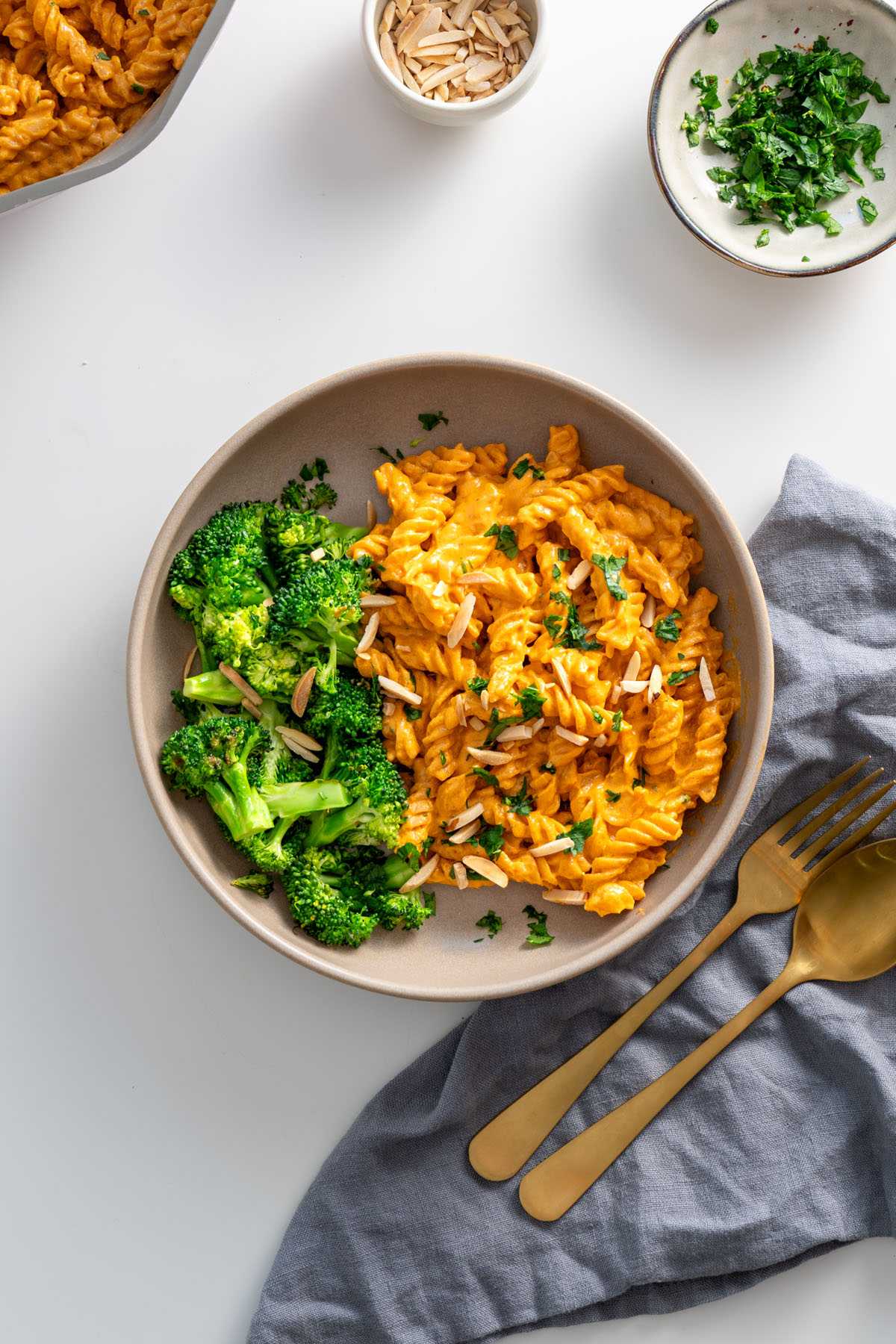 Bowl of high-protein romesco pasta served with steamed broccoli and garnished with fresh parsley and slivered almonds.