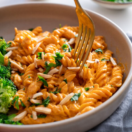 Fork twirling creamy romesco pasta in a bowl with broccoli on the side.