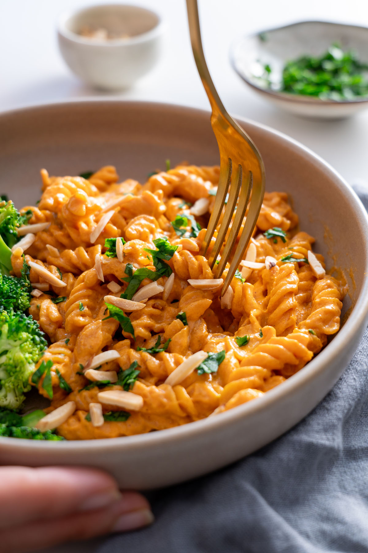 Fork twirling creamy romesco pasta in a bowl with broccoli on the side.