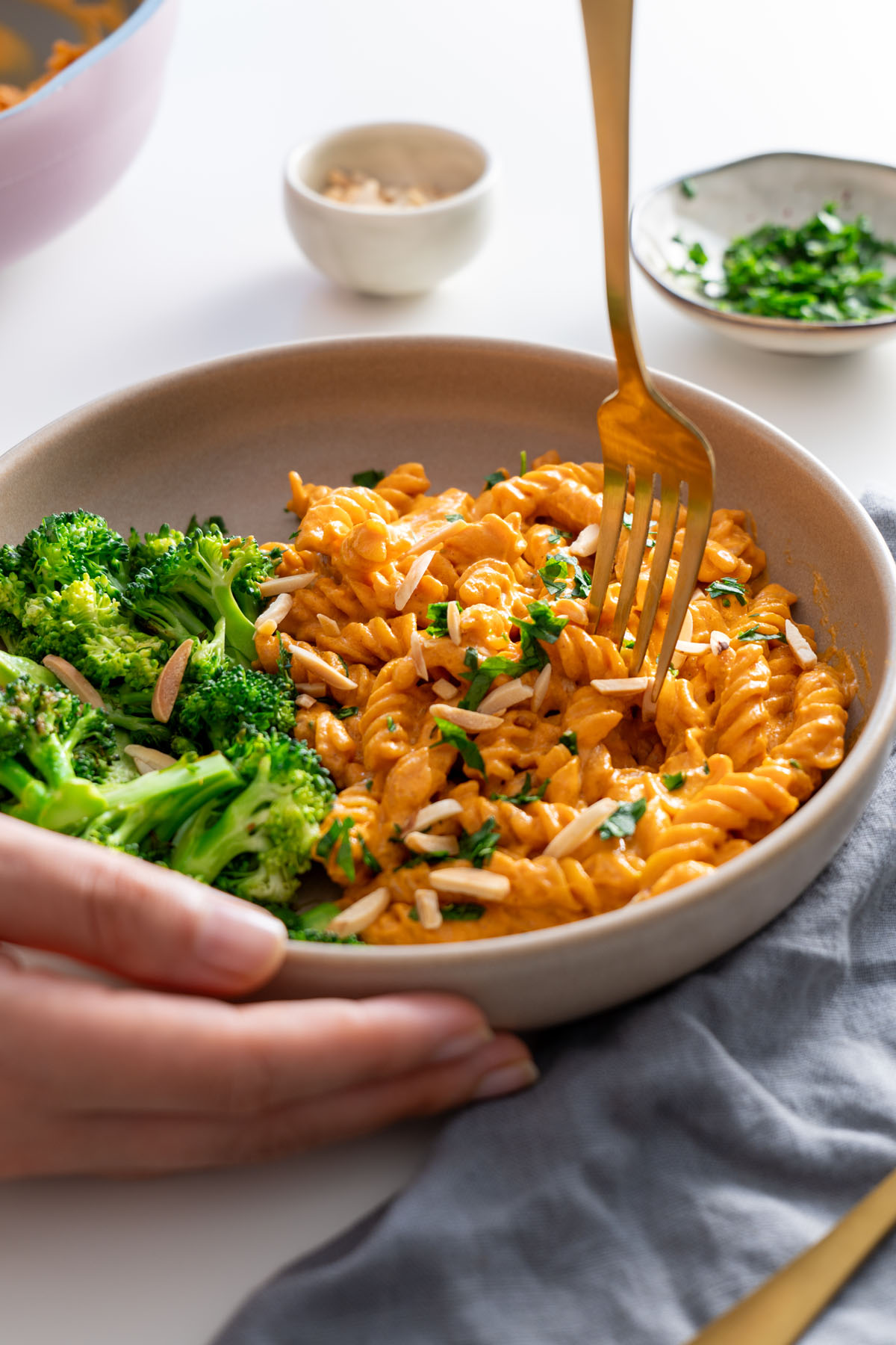 Steamed broccoli and creamy romesco pasta plated with slivered almonds and fresh parsley for garnish.