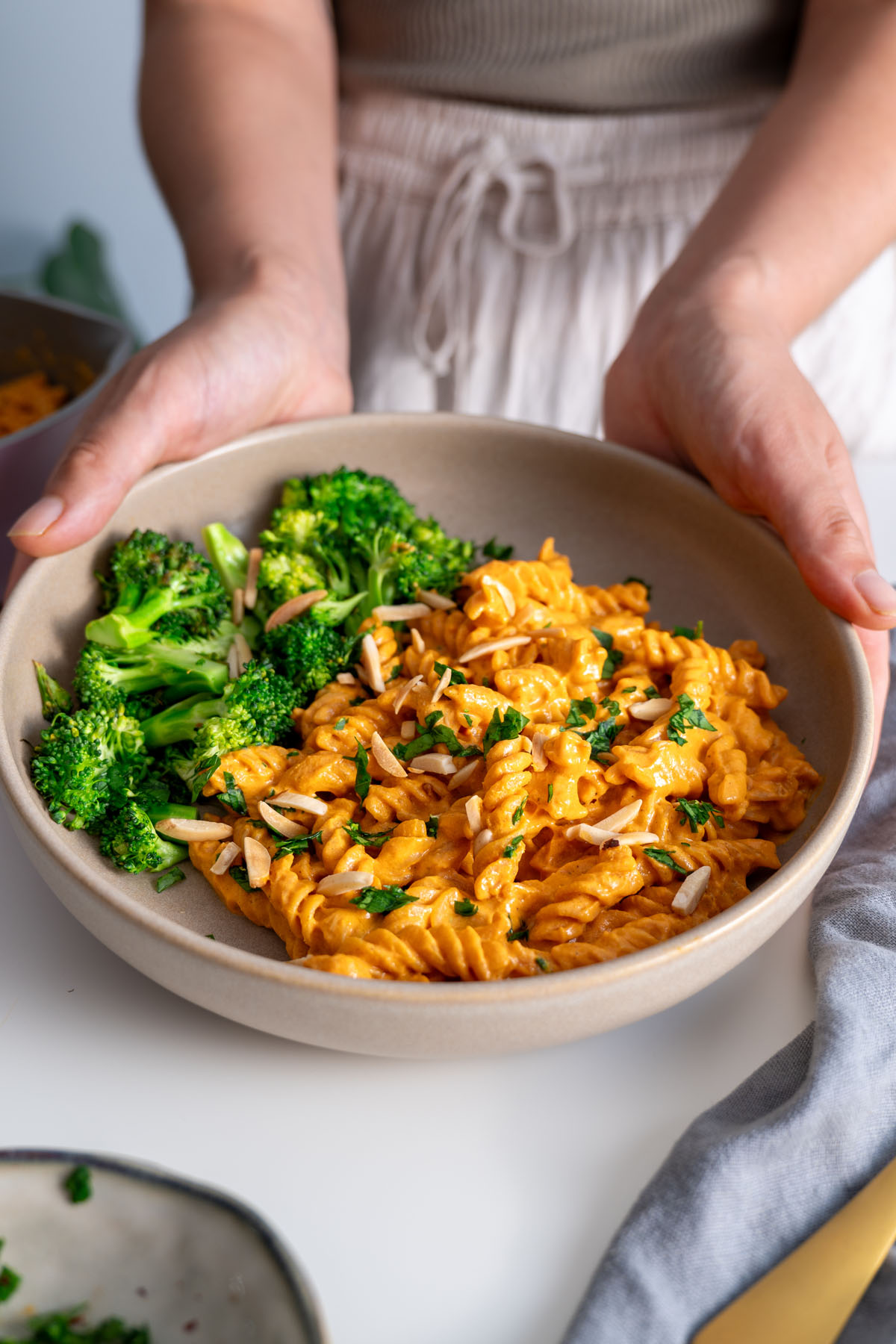 Sarah Cobacho holding a bowl of romesco pasta and broccoli, garnished with parsley and almonds.