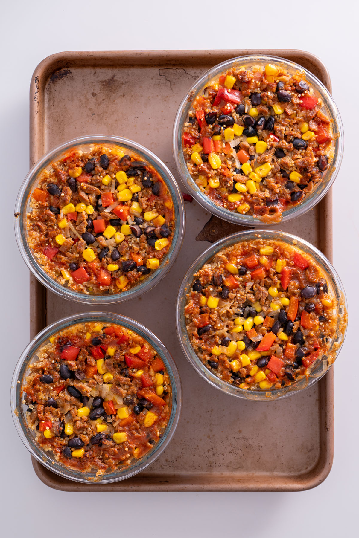 Four glass bowls of oven-baked burrito bowl ingredients arranged on a baking tray after cooking.
