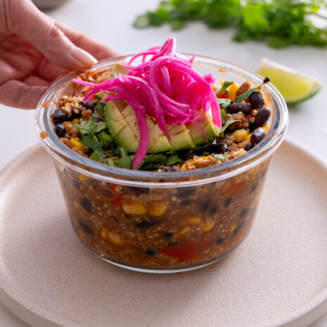 Close-up of an oven-baked burrito bowl with colorful toppings including avocado, pickled onions, and cilantro.