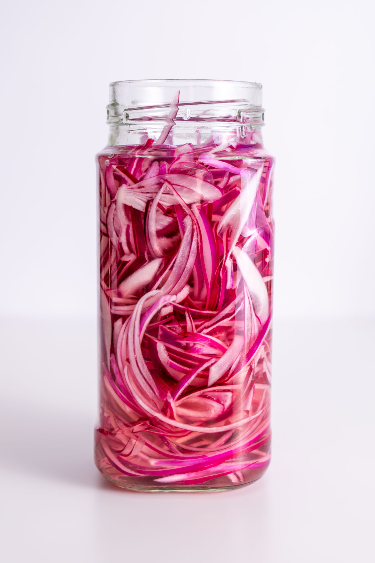 Jar of thinly sliced pink pickled red onions on a white background.