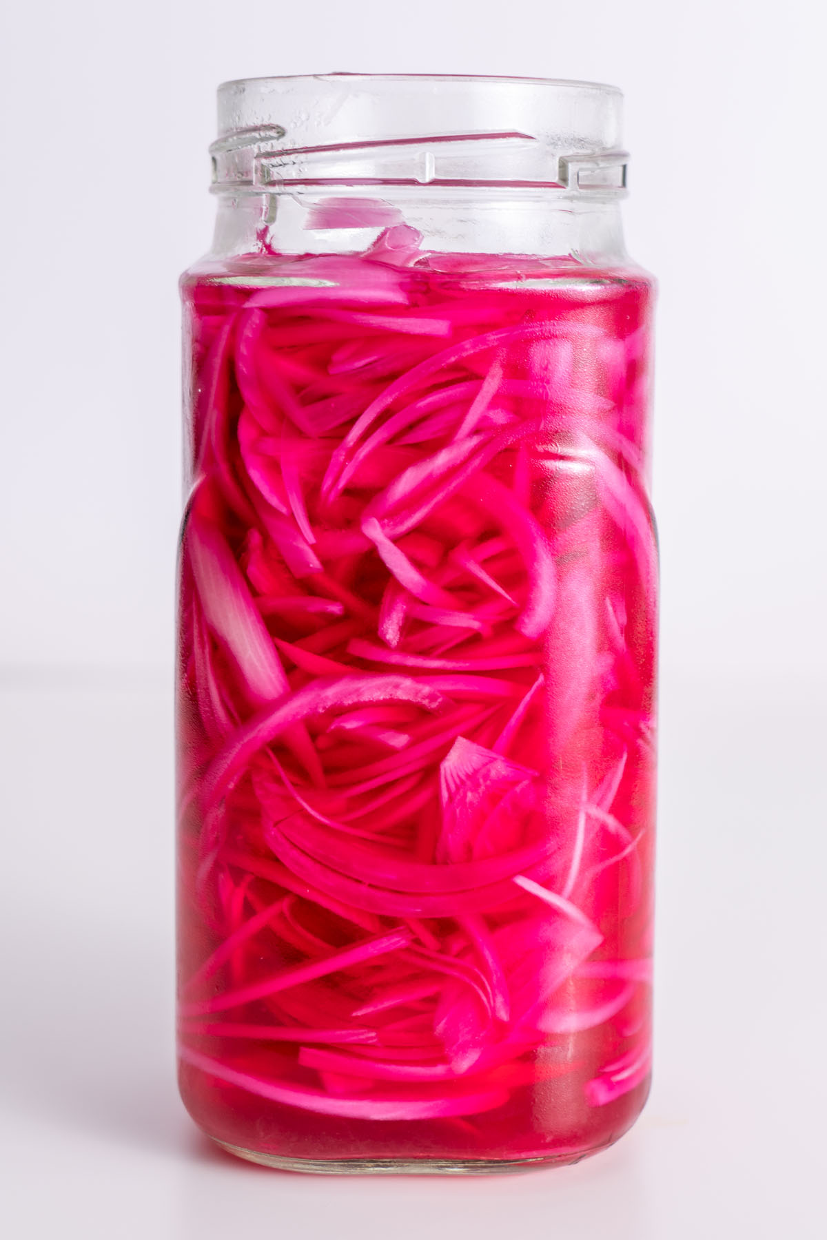 Thinly sliced pickled red onions in a glass jar on a white background.