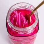 Fork dipped into a jar filled with bright pink pickled red onions.