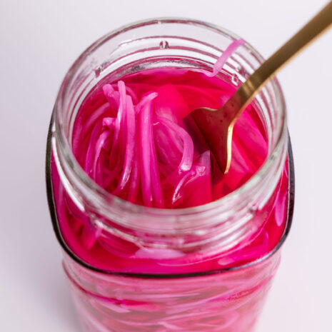 Fork dipped into a jar filled with bright pink pickled red onions.