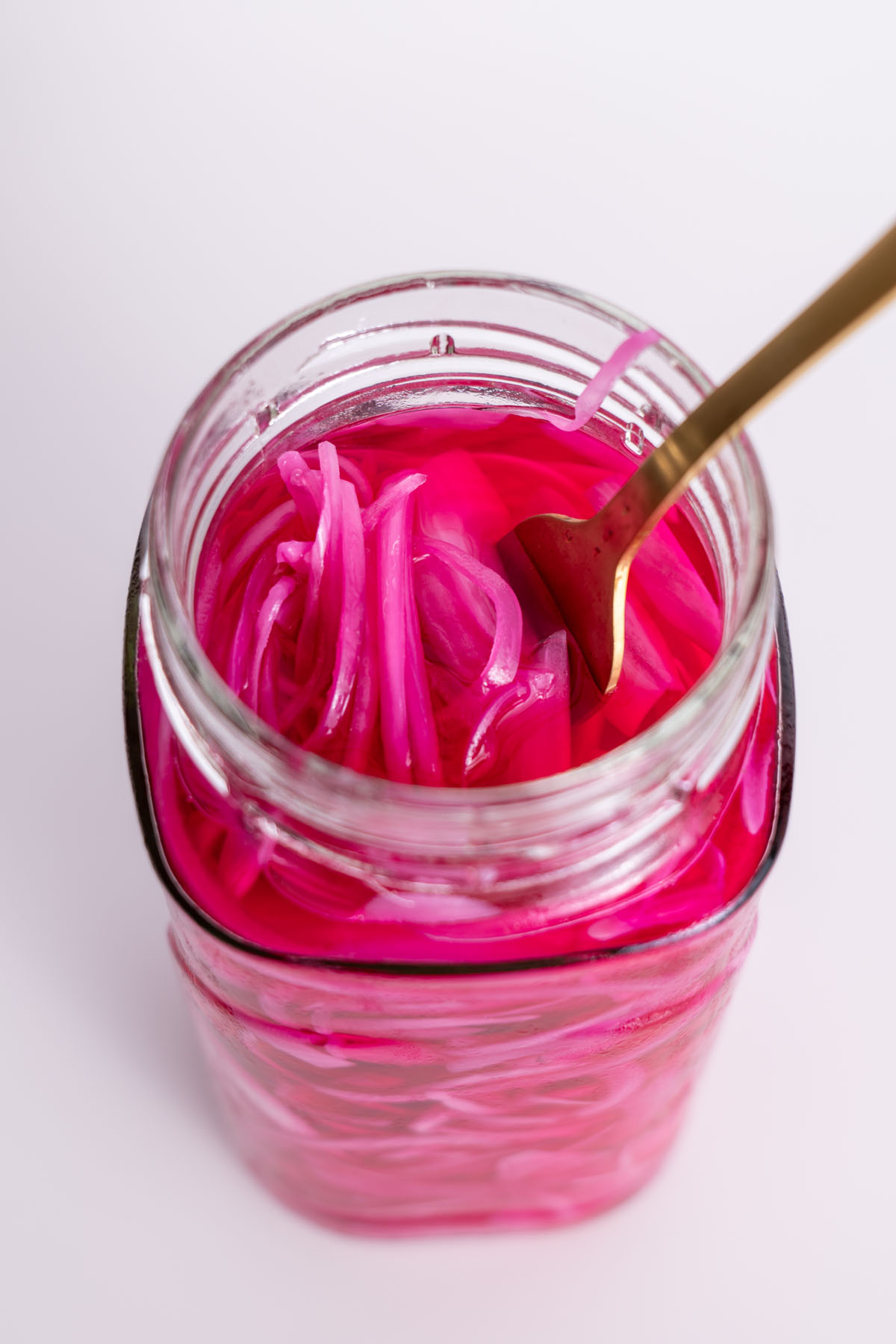 Fork dipped into a jar filled with bright pink pickled red onions.