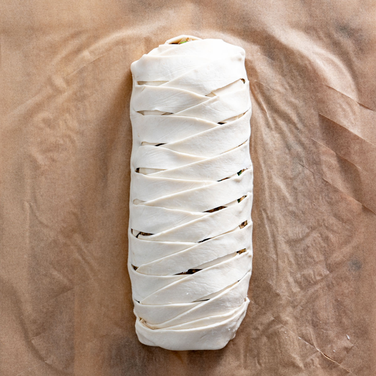 Process shot of braided puff pastry wrapped around the mushroom Wellington filling.