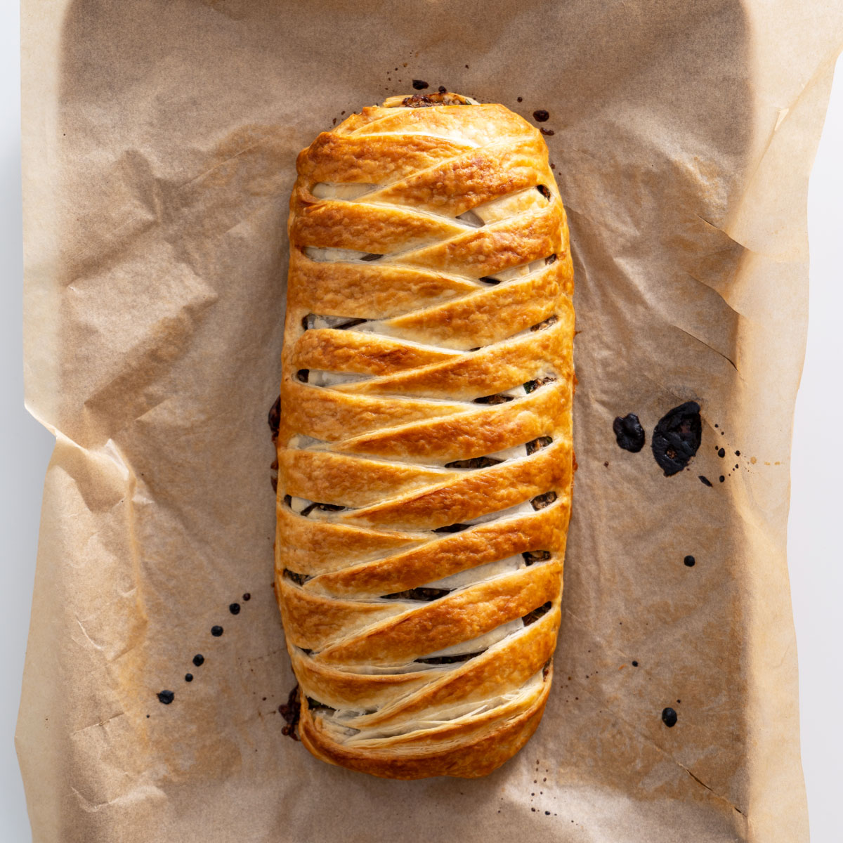 Top-down view of a fully baked braided vegan mushroom Wellington on parchment paper.