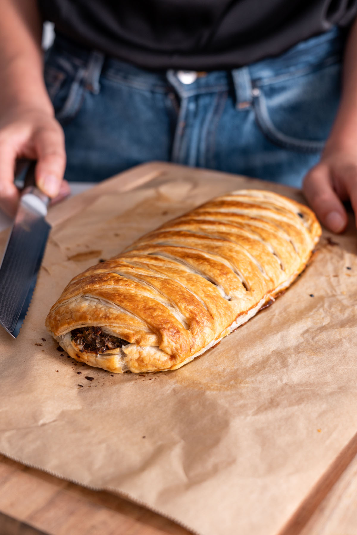 Sarah Cobacho slicing into the vegan mushroom Wellington on a wooden board with parchment paper.