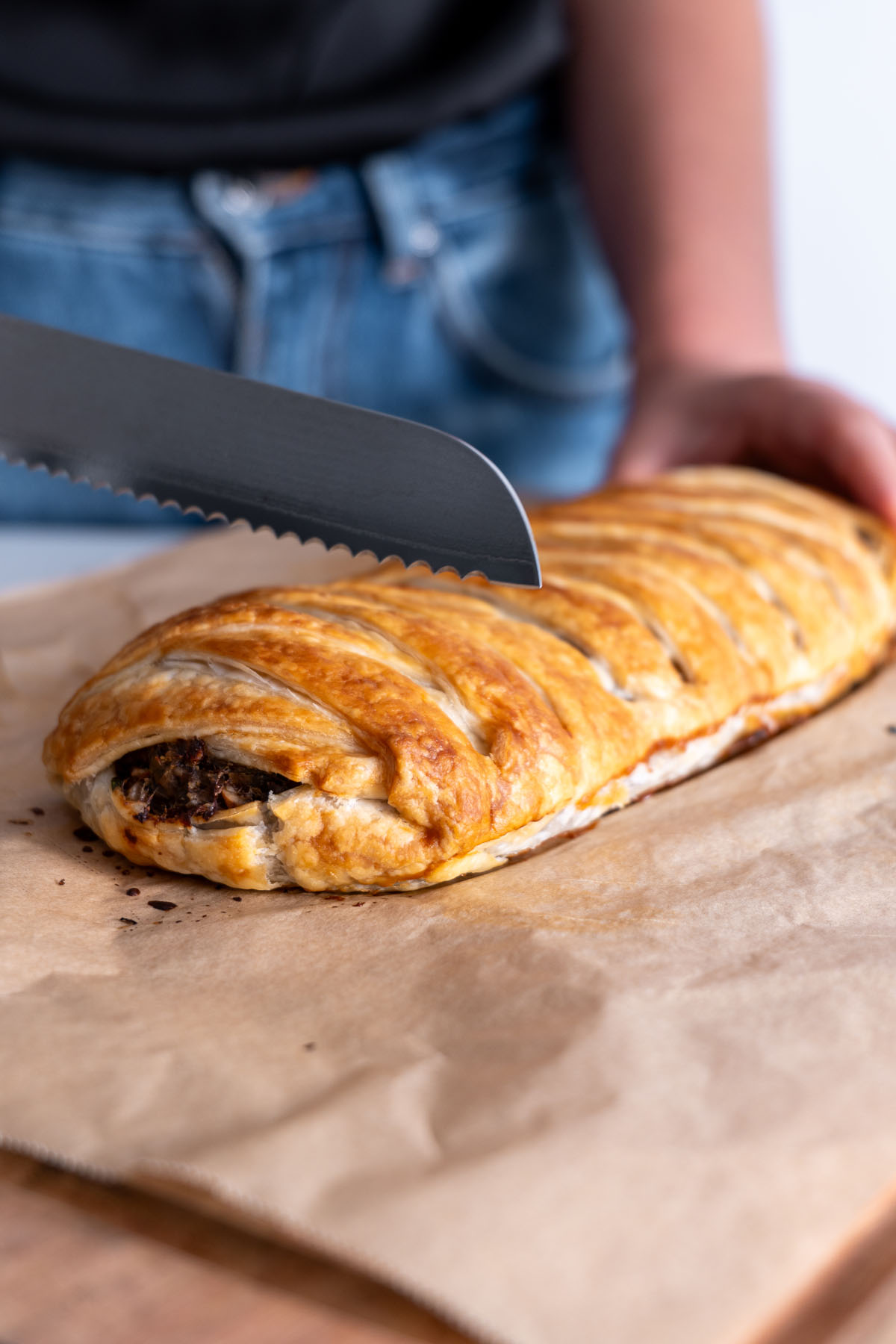 A knife slicing into a vegan mushroom Wellington with a golden crust on parchment paper.