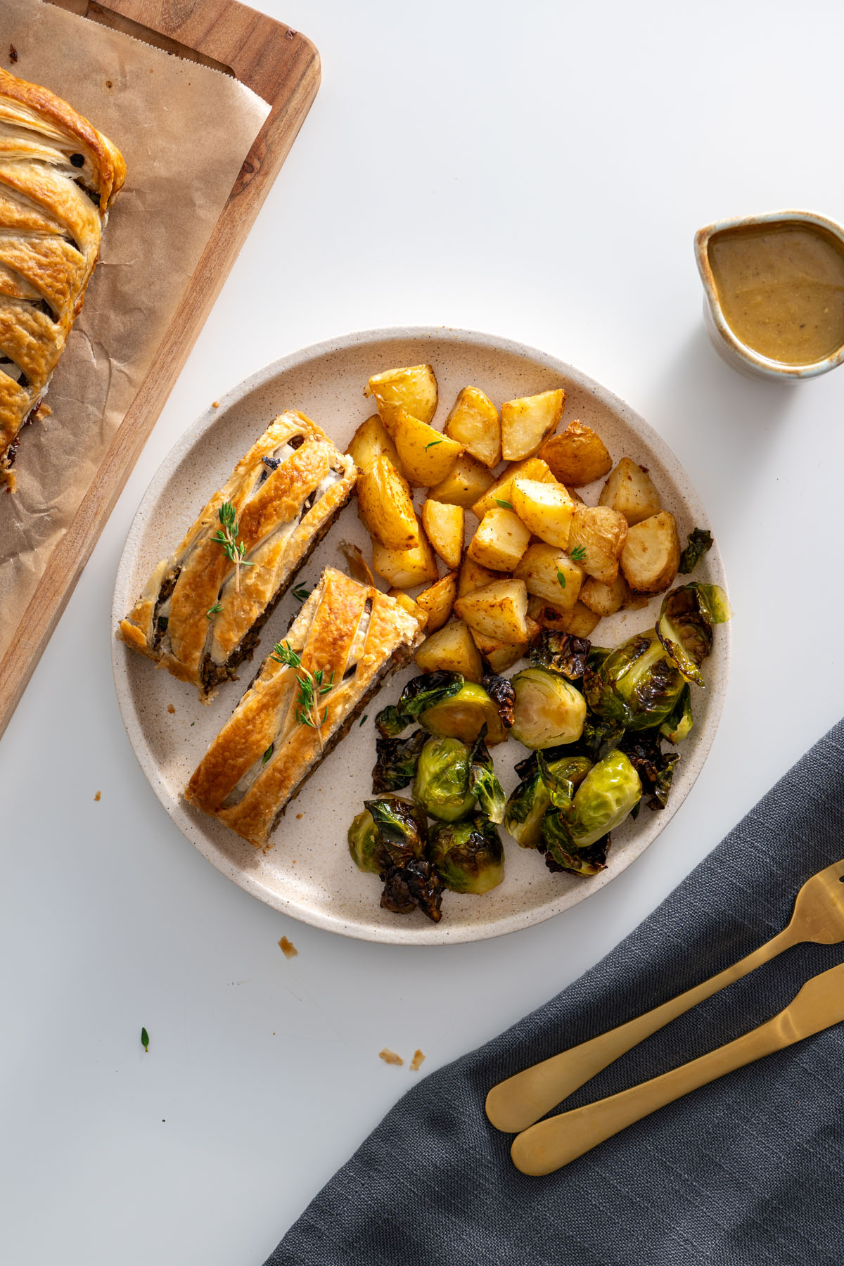 Top-down view of vegan mushroom Wellington slices served with roasted vegetables and gravy on a beige plate.
