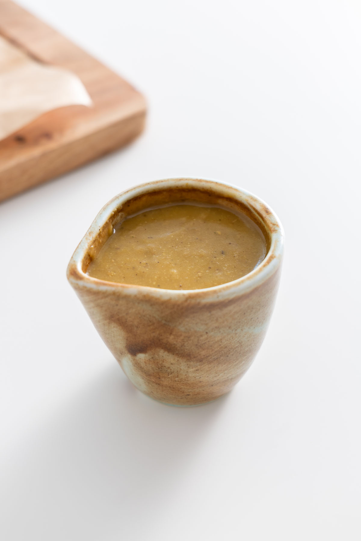 Small ceramic jug of vegetable gravy on a white surface.