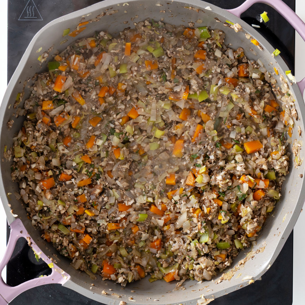 Process shot of sautéed vegetables, mushrooms, and seasonings in a large pan.