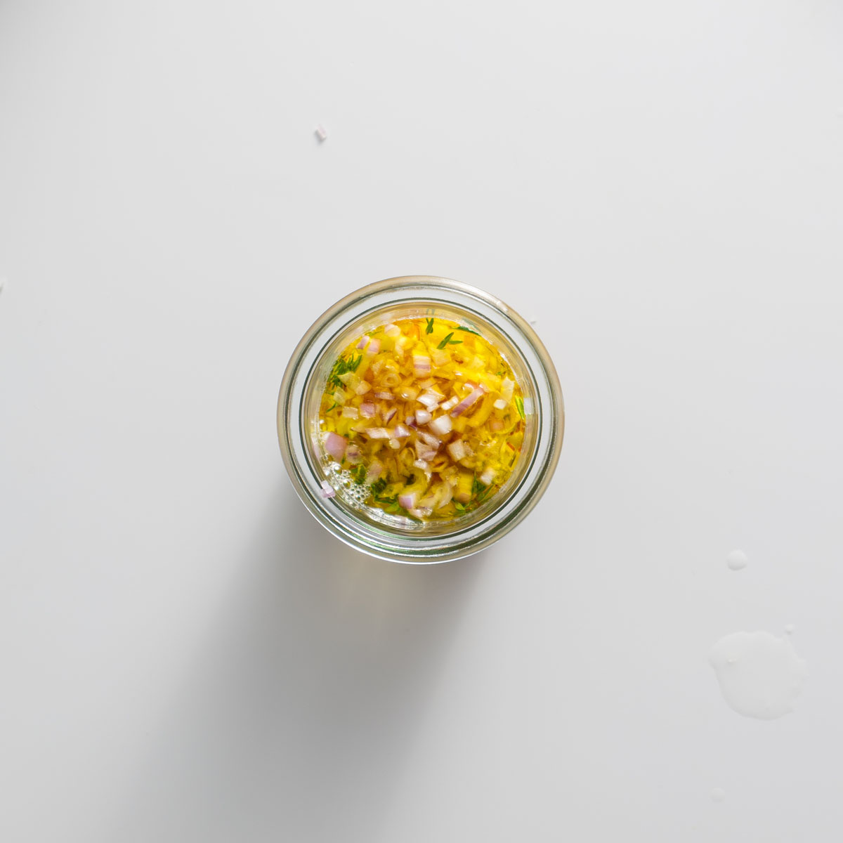 Freshly whisked mustard and herb vinaigrette in a small glass jar on a white surface.