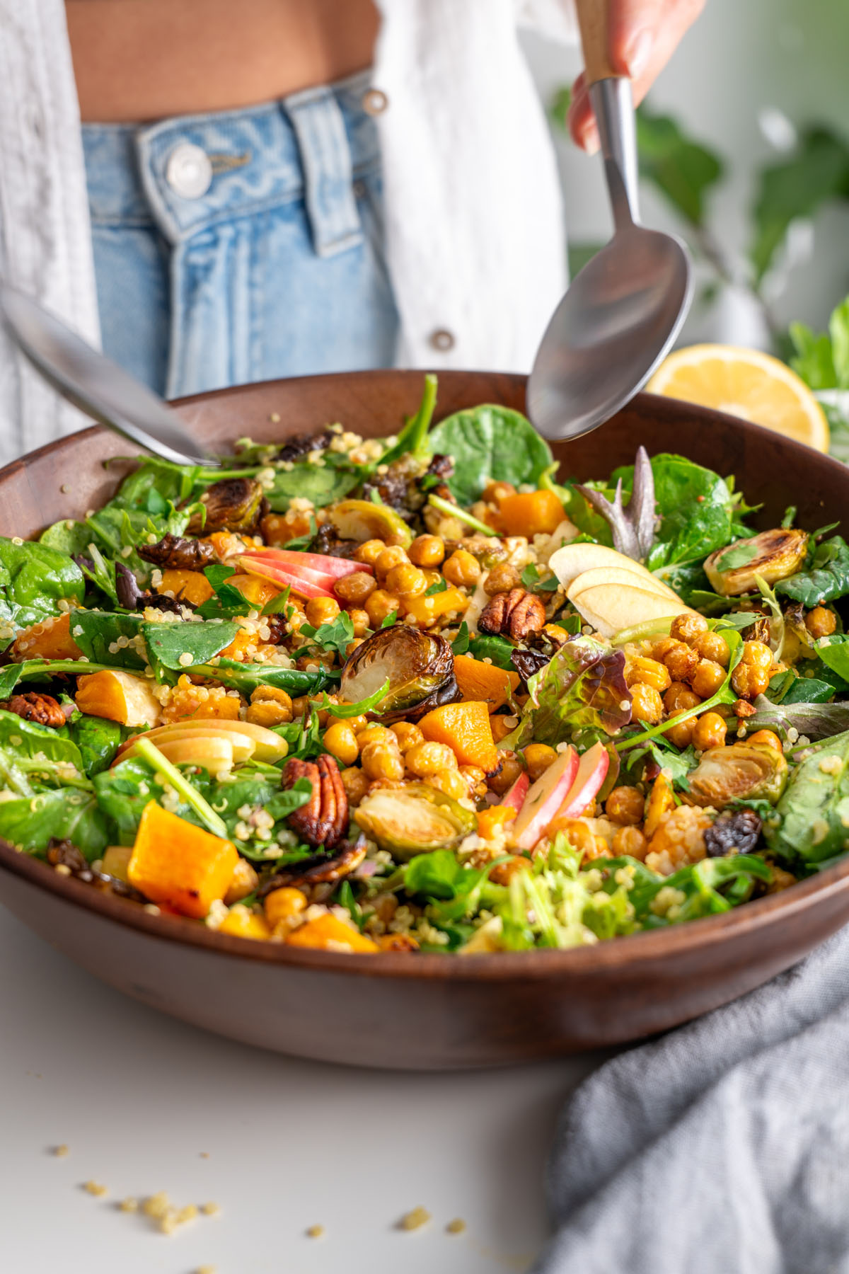 Sarah Cobacho holding salad servers over a vibrant fall salad in a wooden bowl, ready to serve.