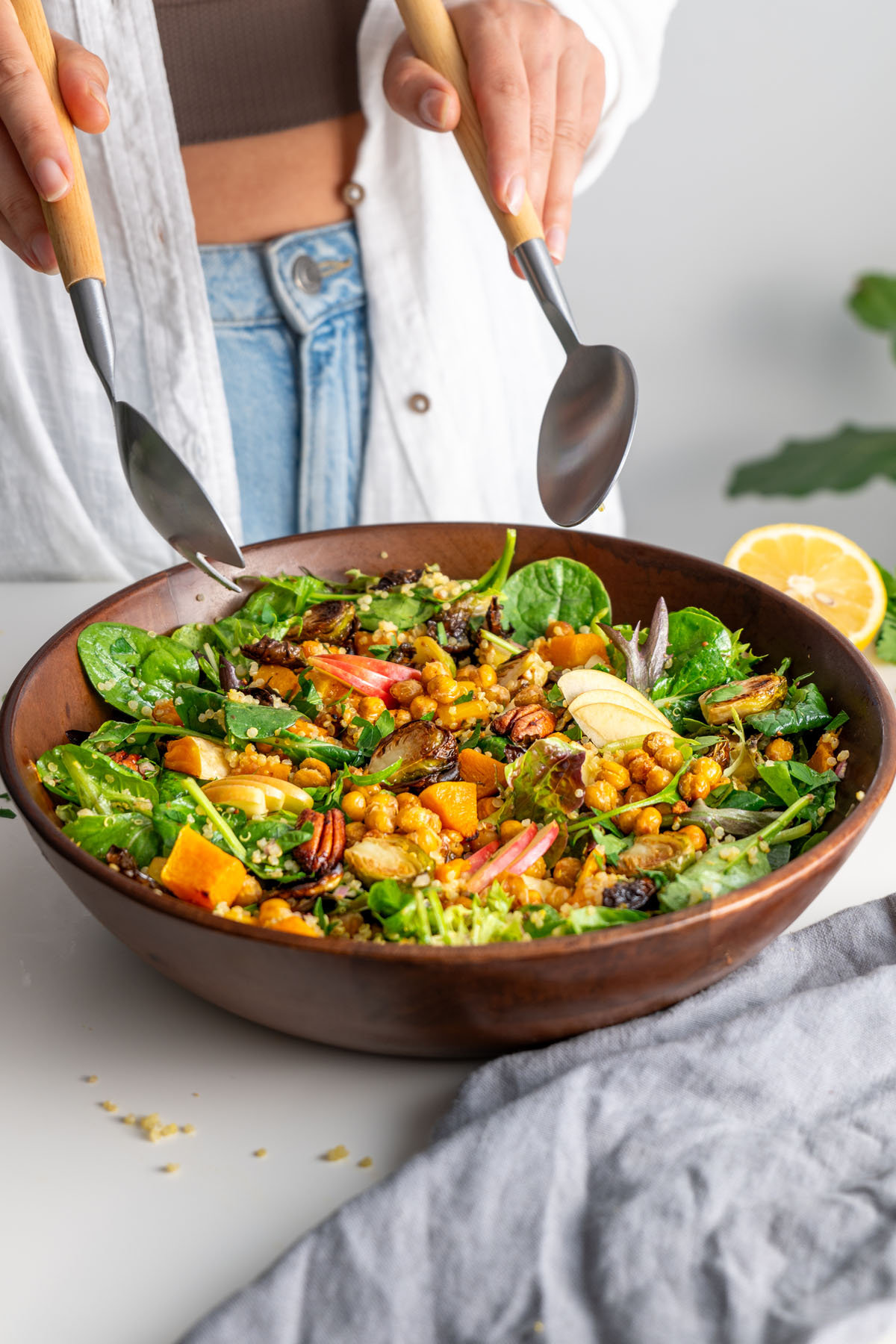 A vibrant fall salad with roasted chickpeas, Brussels sprouts, and butternut squash in a wooden bowl, topped with fresh apple slices.