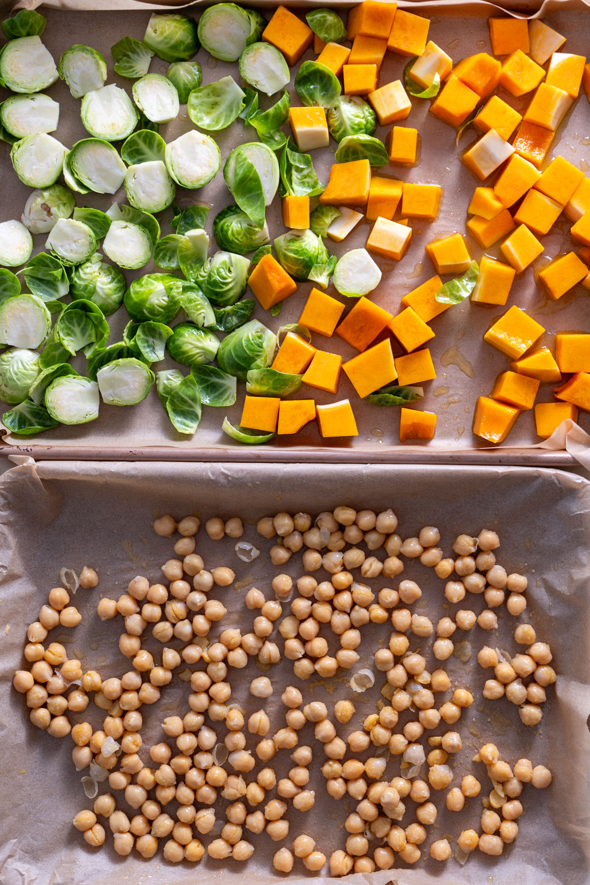 Fresh Brussels sprouts, cubed butternut squash, and chickpeas spread on a baking sheet, ready for roasting.