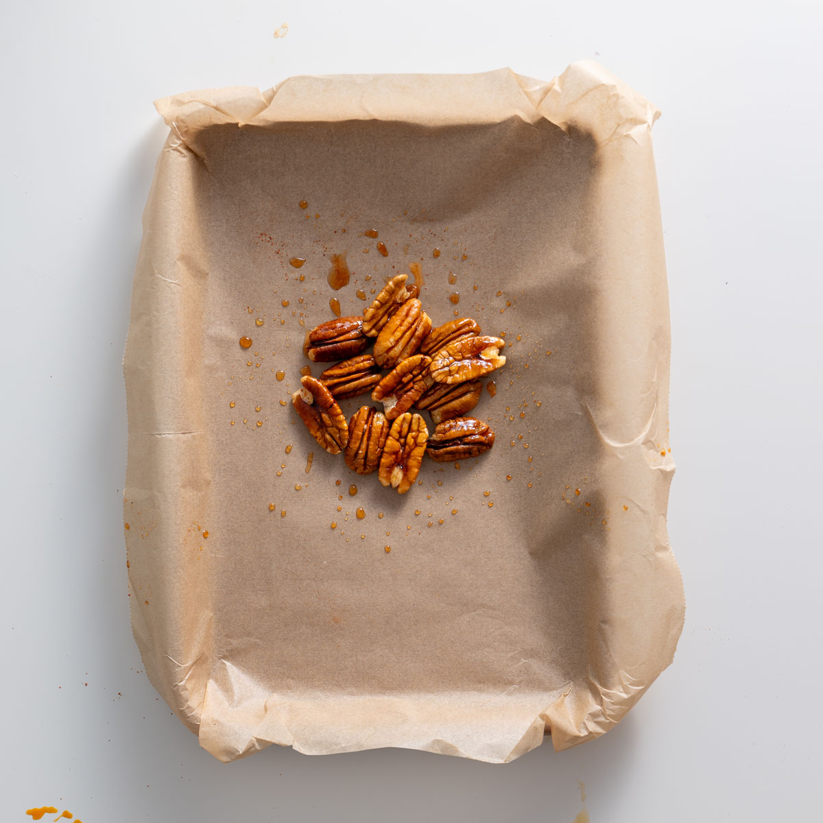 Maple-glazed roasted pecans on parchment paper for a fall salad recipe.
